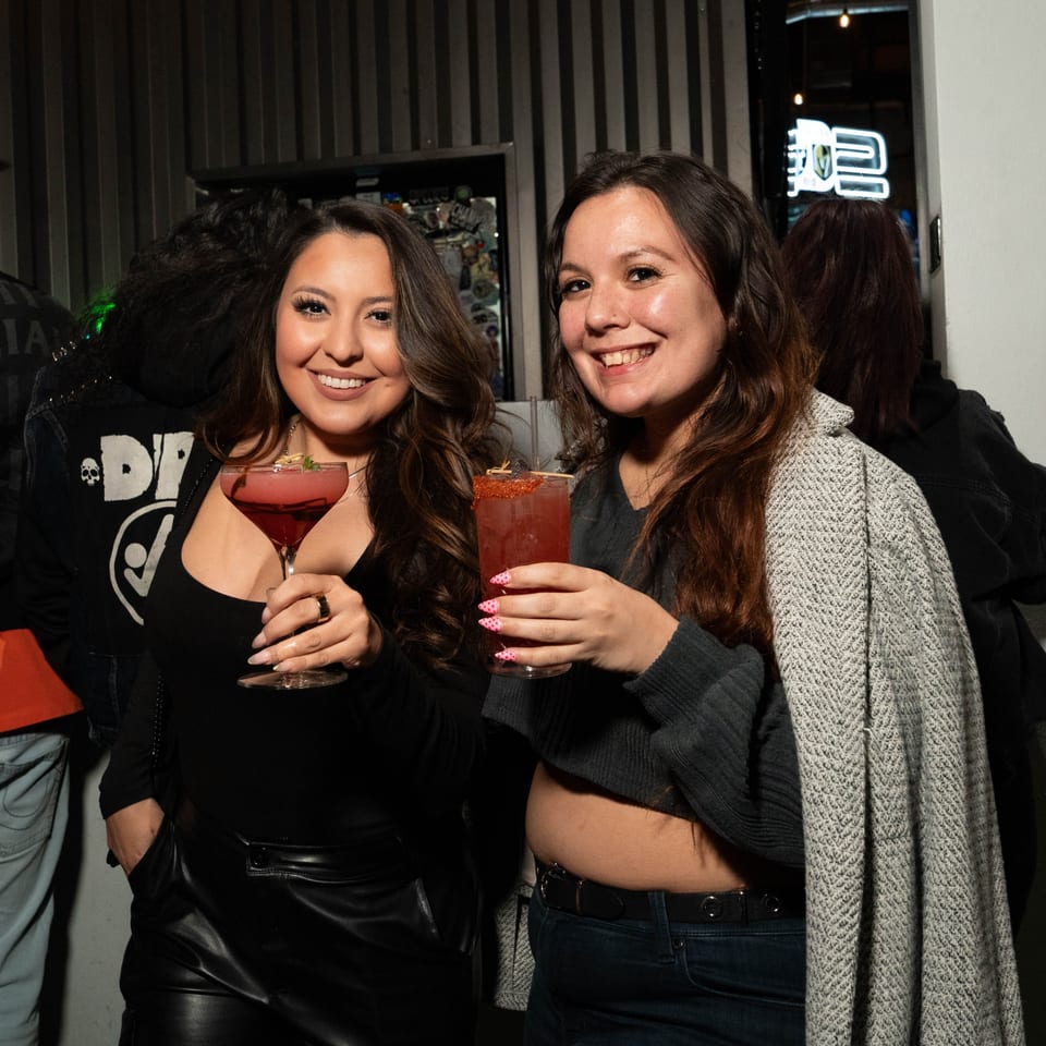 Two smiling women holding red cocktails, enjoying themselves at Servehzah Bottle Shop & Tap Room.