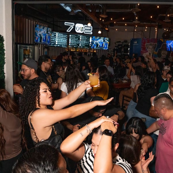 A lively crowd of people dancing and socializing in a dimly lit bar with glowing signs.