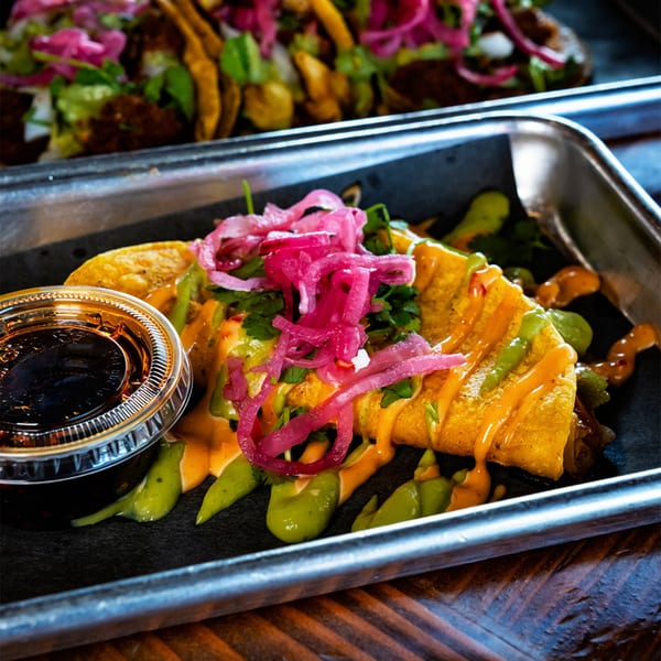 A Servehzah Bottle Shop & Tap Room taco with pickled onions, green and orange sauces, and a side of dark sauce.