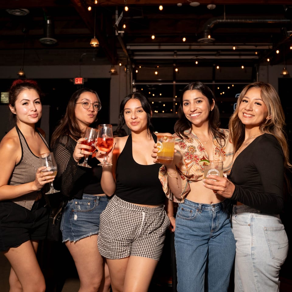 Five women smiling and holding cocktails at Servehzah Bottle Shop & Tap Room.