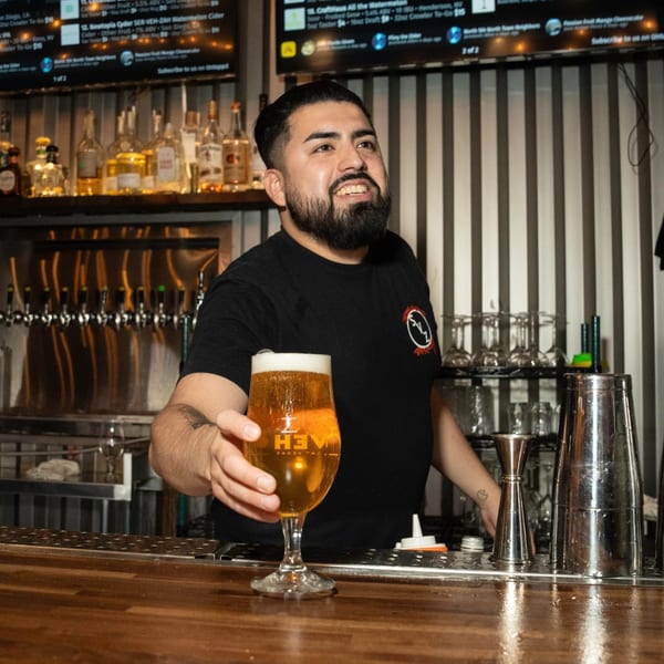 Bartender at Servehzah Bottle Shop & Tap Room serving a glass of beer over the bar.