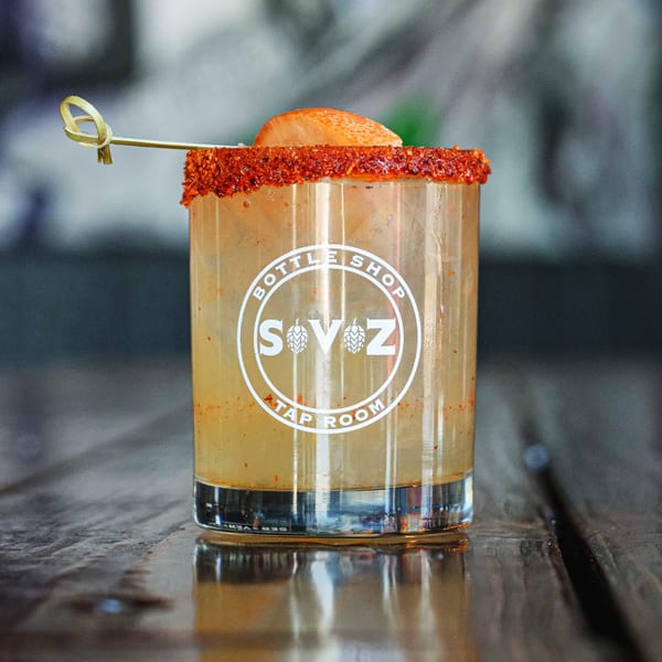 A Servehzah Bottle Shop & Tap Room cocktail with a chili-salt rim and fruit garnish.