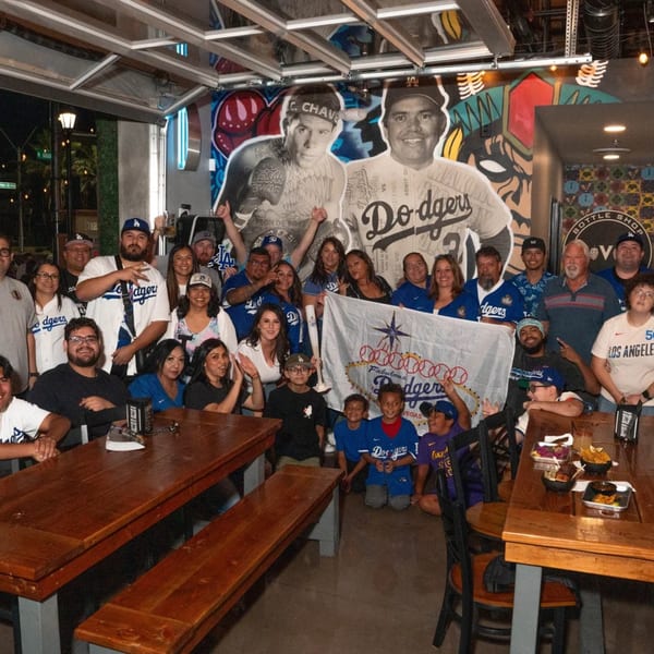 A large group of people, many in Dodgers gear, pose with a flag inside Servehzah Bottle Shop.