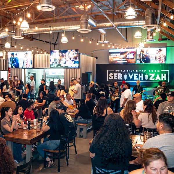 Lively Servehzah Bottle Shop & Tap Room with a band playing and patrons enjoying drinks at tables.