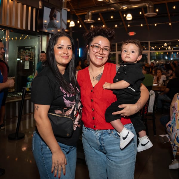 Two women and a baby smiling at the camera inside Servehzah Bottle Shop & Tap Room.