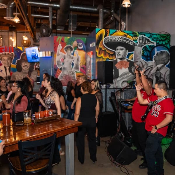 People dancing and enjoying drinks at Servehzah Bottle Shop & Tap Room, with colorful murals in the background.