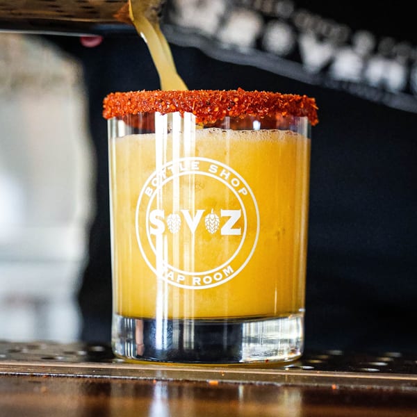 A Servehzah Bottle Shop & Tap Room glass with a chili-rimmed michelada being poured.