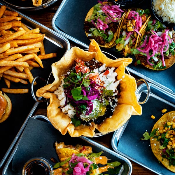 Overhead view of Servehzah's bar food, including tacos, a taco salad bowl, and french fries.