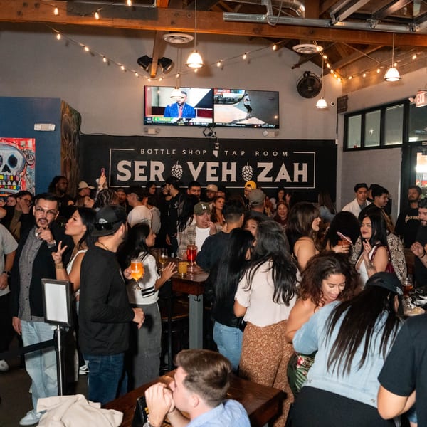 A lively crowd of people socializing and drinking at Servehzah Bottle Shop & Tap Room.