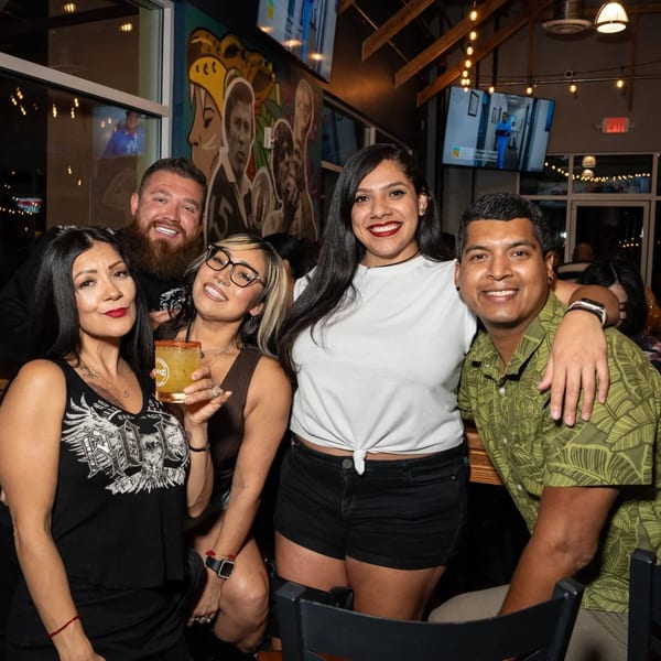 Five smiling friends, three women and two men, pose together at Servehzah Bottle Shop & Tap Room.