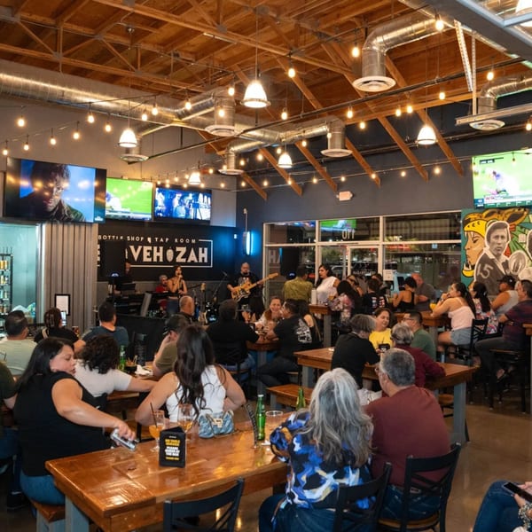 A lively Servehzah Bottle Shop & Tap Room with a band playing and patrons enjoying drinks.